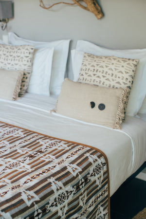 Blanket neatly spread over the surface of a bed with white sheets and white and beige pillows