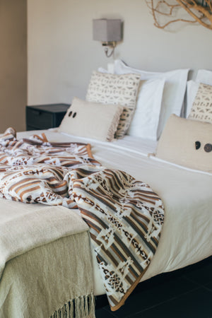 Celtic geometric pattern in white and browns, on reverse side it's on a bed with pillows on the background