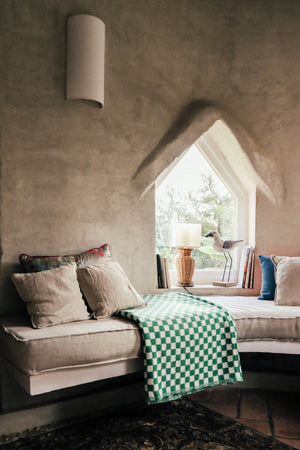 Checkered blanket in green folded flat on a windowsill seat amongst cushions by the wondow