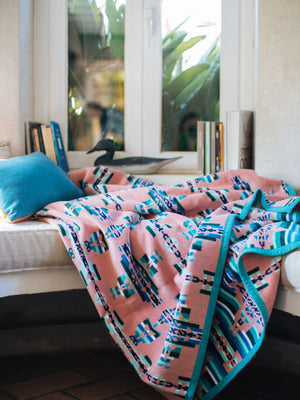 Pink and Green blanket on a window seat with geometric symbol of mother and child 
