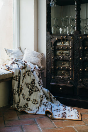 Celtic geometric pattern blanket hanging from window seat stretching on the tiled terracotta floor, on the background is a vintage victorian bar chest with wine glasses
