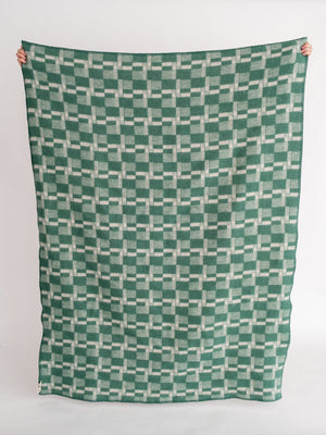 Green and white patterned blanket held up against a white background