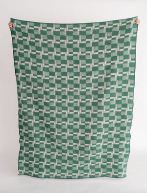 Green and white patterned blanket held up against a white background